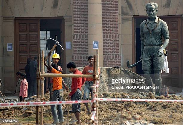 In this picture taken on December 6 Indian labourers are watched over by a statue of Indian hockey player Dhyan Chand at The Dhyan Chand National...