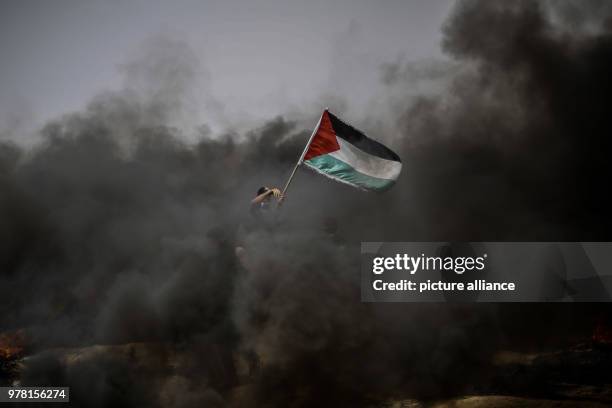 Dpatop - A Palestinian protester holds his national flag during clashes with Israeli security forces along the Israel-Gaza border, in Khan Younis,...