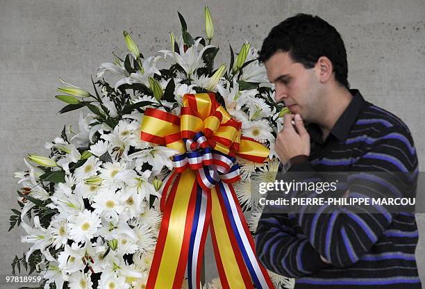 Man stand next to a wreath of flowers during a ceremony on March 18, 2010 in Boadilla del Monte, near Madrid, to pay tribute to French policeman Jean...