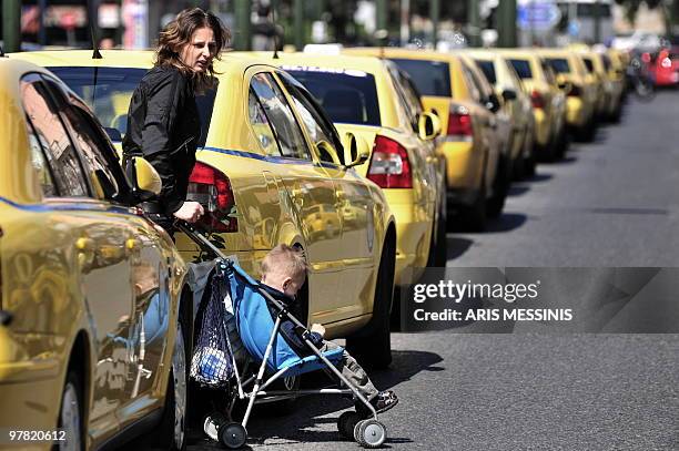 Woman with her baby walk between parked taxis during a 24hours strike of Greek taxi drivers in Athens on March 18, 2010. AFP PHOTO / Aris Messinis