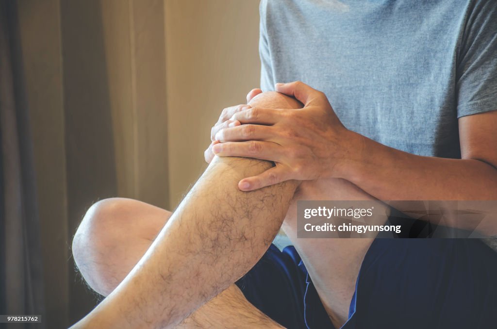 Closeup Mann Hand, die Knie mit Schmerzen im Bett, Gesundheitswesen und medizinische Konzept