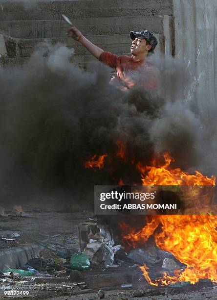 Smoke billows from burning tyres as a Palestinian youth hurls stones at Israeli soldiers during clashes in the West Bank refugee camp of Qalandia on...