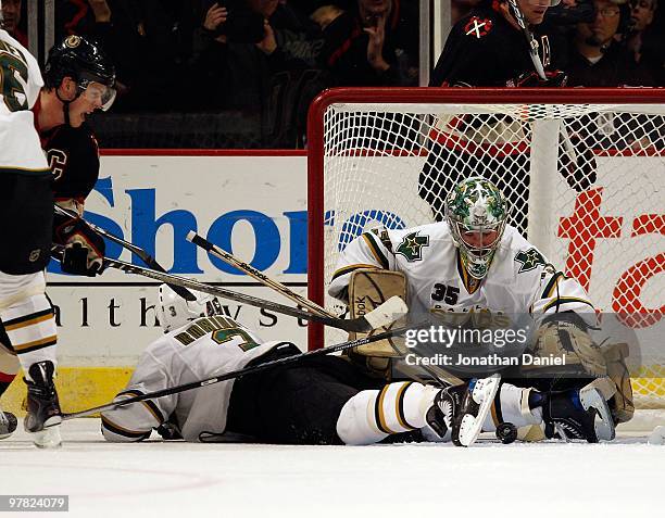 Marty Turco of the Dallas Stars reaches for the puck over teammate Stephane Robidas on a shot by Jonathan Toews of the Chicago Blackhawks during a...