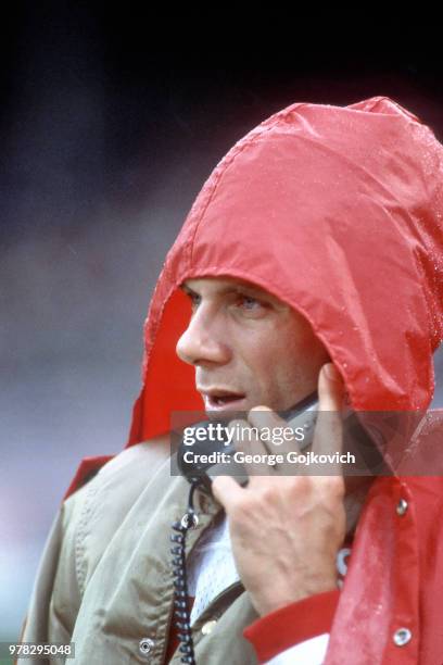 Quarterback Joe Montana of the San Francisco 49ers takes cover from the rain while talking on the phone to coaches who were stationed overhead in the...
