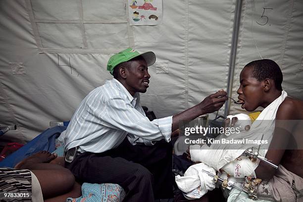 Martin Joesph, earthquake survivor, is fed by this father Jules Joseph at the Red Cross medical observation tent inside General Hospital on February...