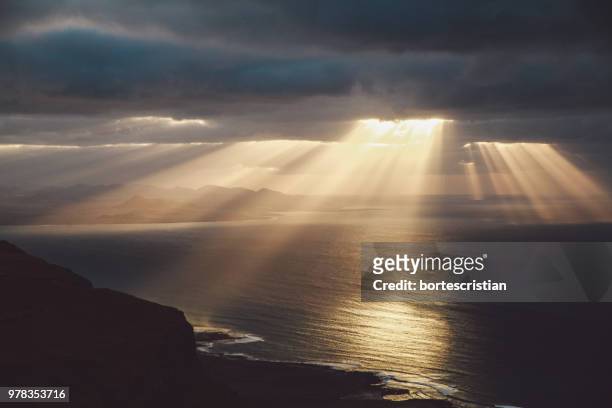 sunlight streaming through clouds over sea - bortes fotografías e imágenes de stock