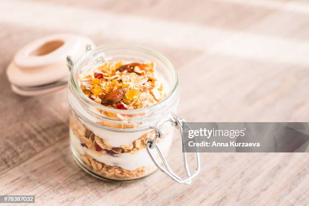 traditional breakfast from switzerland. jar of homemade muesli bircher with plain yogurt, toasted oat flakes, almonds, peanuts, dried fruits and honey on a wooden table, selective focus. organic food. - raisin bran stock pictures, royalty-free photos & images