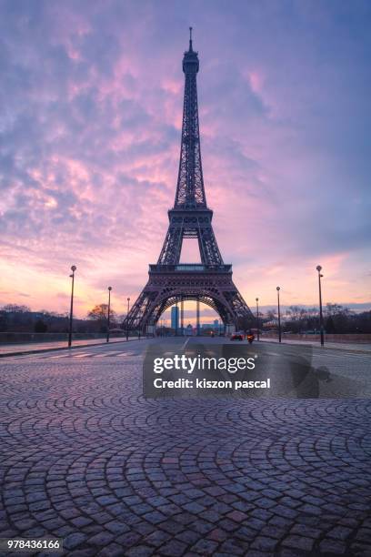 the eiffel tower in paris with paved empty road during a colorful sunrise , france - tour eiffel photos et images de collection