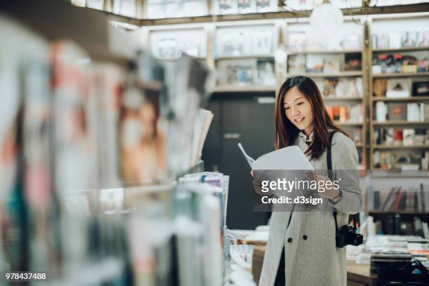 professional female photographer with camera reading books in book store for some inspirations - book shop stock-fotos und bilder