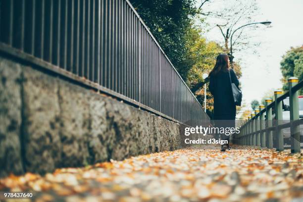rear view of young woman walking in city street on the way to work on a breezy autumn morning - business air travel photos et images de collection