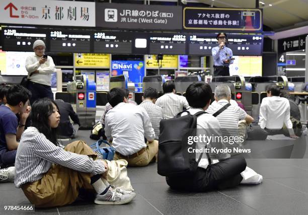 Passengers sit in front of a gate of JR Kyoto Station on June 18, 2018 waiting for train service to resume. Train operations were suspended due to a...