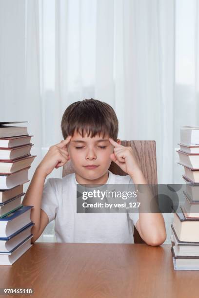 close-up of boy, 8-9 years, trying to concentrate surrounded by stacks of books - boys only caucasian ethnicity 6 7 years stock-fotos und bilder