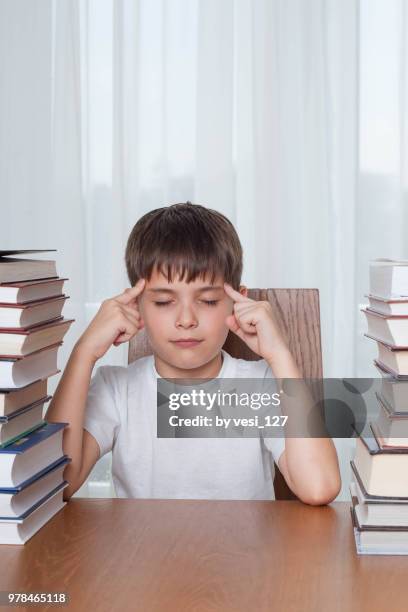 close-up of boy, 8-9 years, trying to concentrate surrounded by stacks of books - boys only caucasian ethnicity 6 7 years stock pictures, royalty-free photos & images