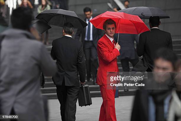 man wearing red suit, holding umbrella in city - si distingue fra la folla foto e immagini stock