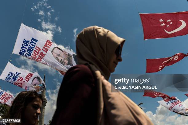 People walk past presidential campaign banners of Turkey's incumbent president and campaign flags of the conservative Saadet Party on June 19, 2018...