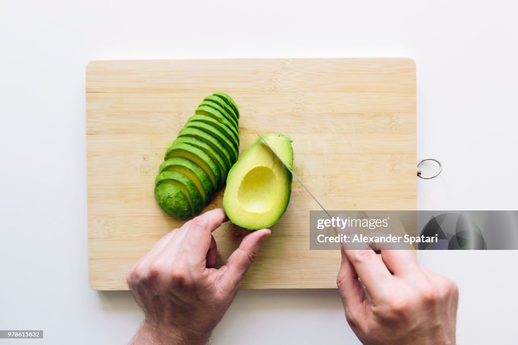 Man cutting avocado on a wooden cutting board, personal perspective directly above view