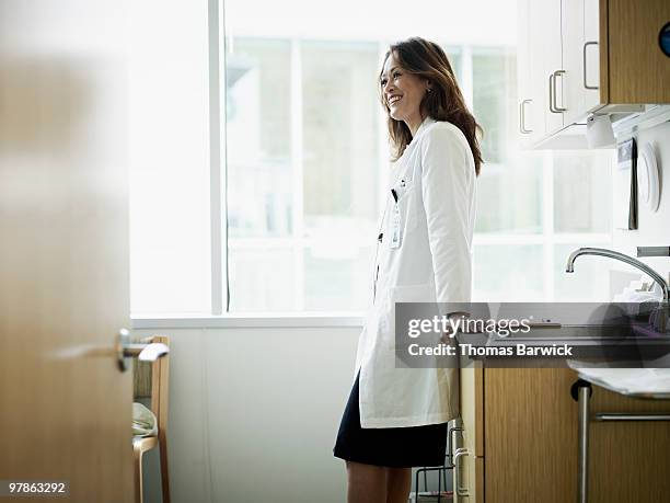 female doctor leaning against counter in exam room - women with health faucet stock pictures, royalty-free photos & images