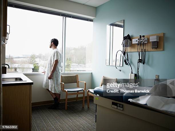 male patient in gown waiting in exam room - adult male hospital bed stock-fotos und bilder