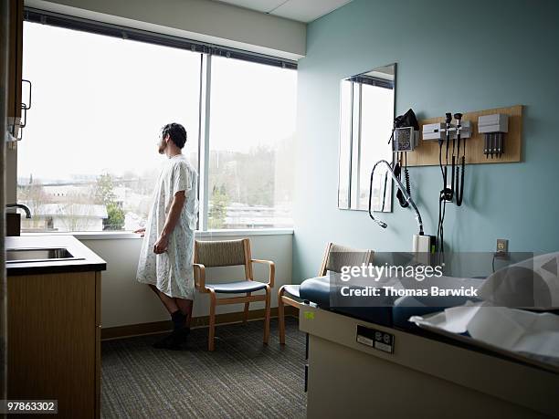 male patient in gown waiting in exam room - hospital gown imagens e fotografias de stock