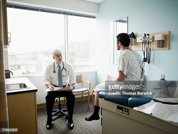 male patient and doctor in discussion in exam room - doctor sitting stock pictures, royalty-free photos & images