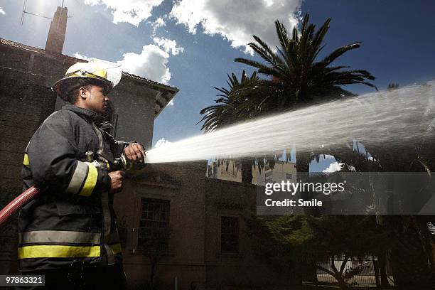 fireman spraying hose - brandslang stockfoto's en -beelden