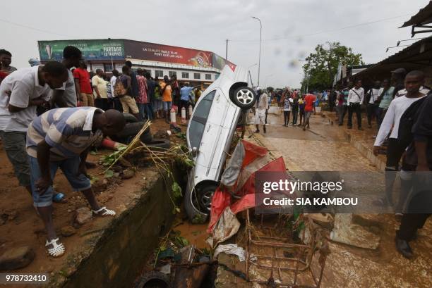 Pedestrians look at the wreckage of a vehicle lodged in a storm drain on a street in Abidjan on June 19 in which a man was reportedly found dead...