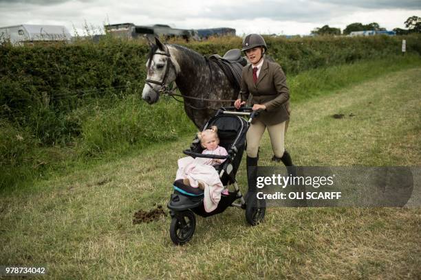 Woman pushes a pushchair as she leads a horse adjacent to a showjumping ring on the first day of The Royal Cheshire County Show at Tabley, near...