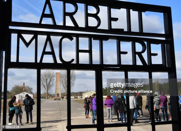 February 2018, Germany, Oranienburg: Visitors walk past the cast iron entrance gate with the writing 'Arbeit macht frei' at the memorial site of...