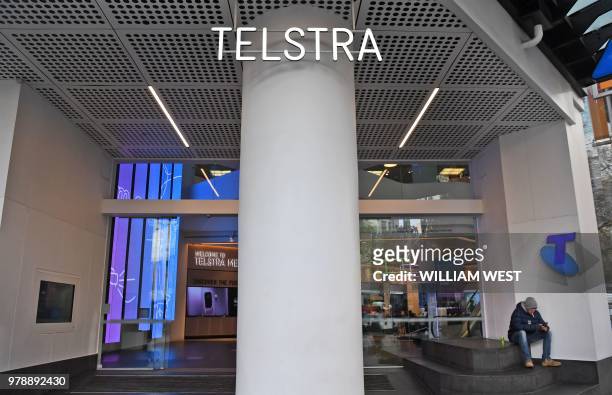 Man sits by the entrance to a Telstra store on Melbourne's central business district on June 20, 2018. - Australia's dominant telecommunications...