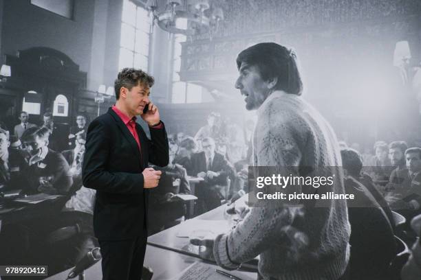 March 2018, Germany, Wolfsburg: The director of the art museum, Ralf Beil, on his phone at the exhibition "Robert Lebeck 1968". In the background is...