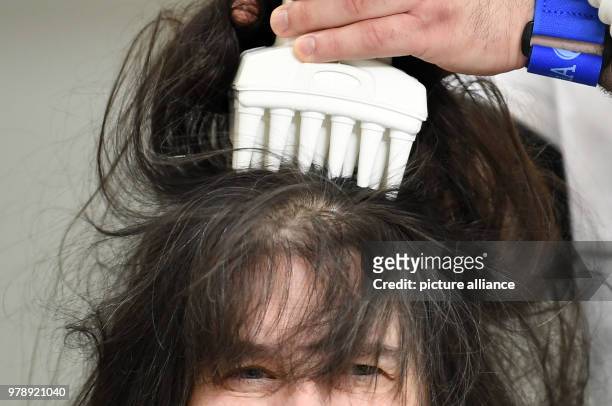 March 2018, Germany, Berlin: Naram Shakra kills the head lice of the customer Monika Beloch at the anti lice salon "Bye bye Laeuse" with hot air....