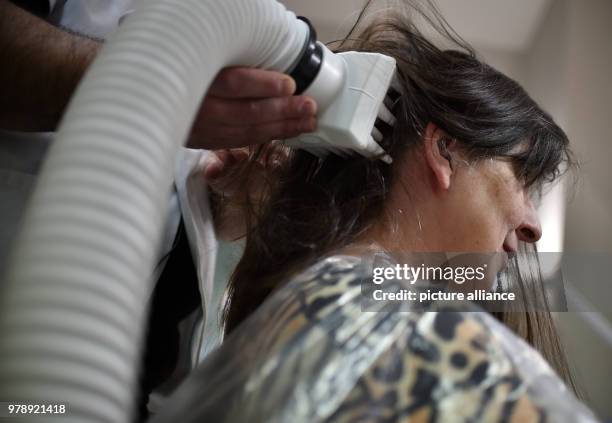 March 2018, Germany, Berlin: Naram Shakra kills the head lice of the customer Monika Beloch at the anti lice salon "Bye bye Laeuse" with hot air....