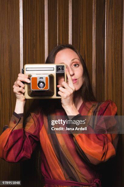 retro 1970s woman taking photo with camera vintage instant camera - funny photographer studio stock-fotos und bilder