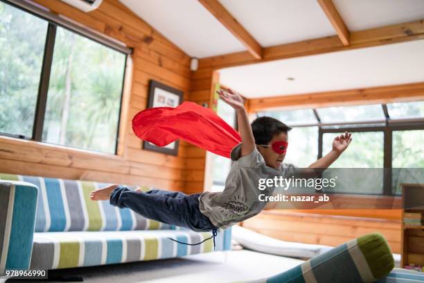 kid with superhero mask jumping on sofa. - superhero stock pictures, royalty-free photos & images