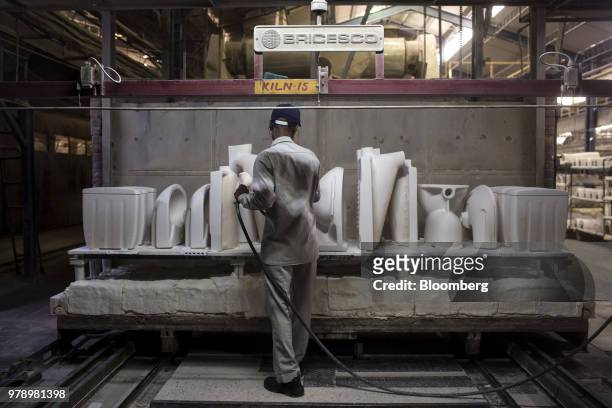 An employee uses an air gun to remove dust and dirt from kiln-fired toilet and wash basin parts at the HSIL Ltd. Factory in Bahadurgarh, Haryana,...