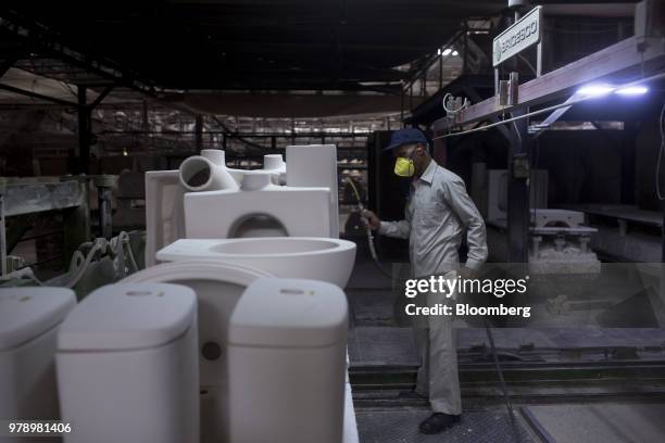 An employee uses an air gun to remove dust and dirt from kiln-fired toilet and wash basin parts at the HSIL Ltd. Factory in Bahadurgarh, Haryana,...