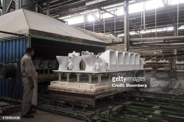 An employee watches a platform truck laden with glazed toilets enter a kiln at the HSIL Ltd. Factory in Bahadurgarh, Haryana, India, on Monday, June...