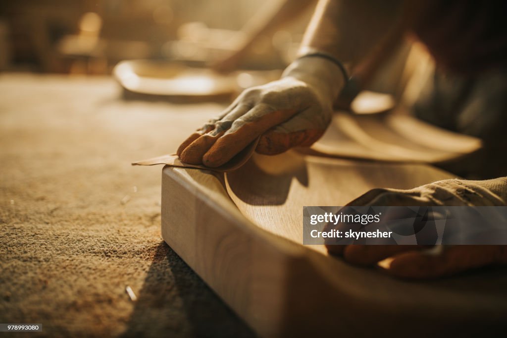 Feche de carpinteiro irreconhecível restaurando uma madeira com papel da areia.