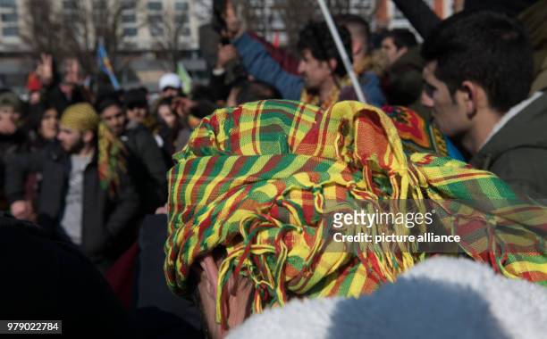 March 2018, Germany, Berlin: A man wears the Kurdish flag as a headscarf in a demonstration sparked by Turkish aggressions in the Syrian province of...