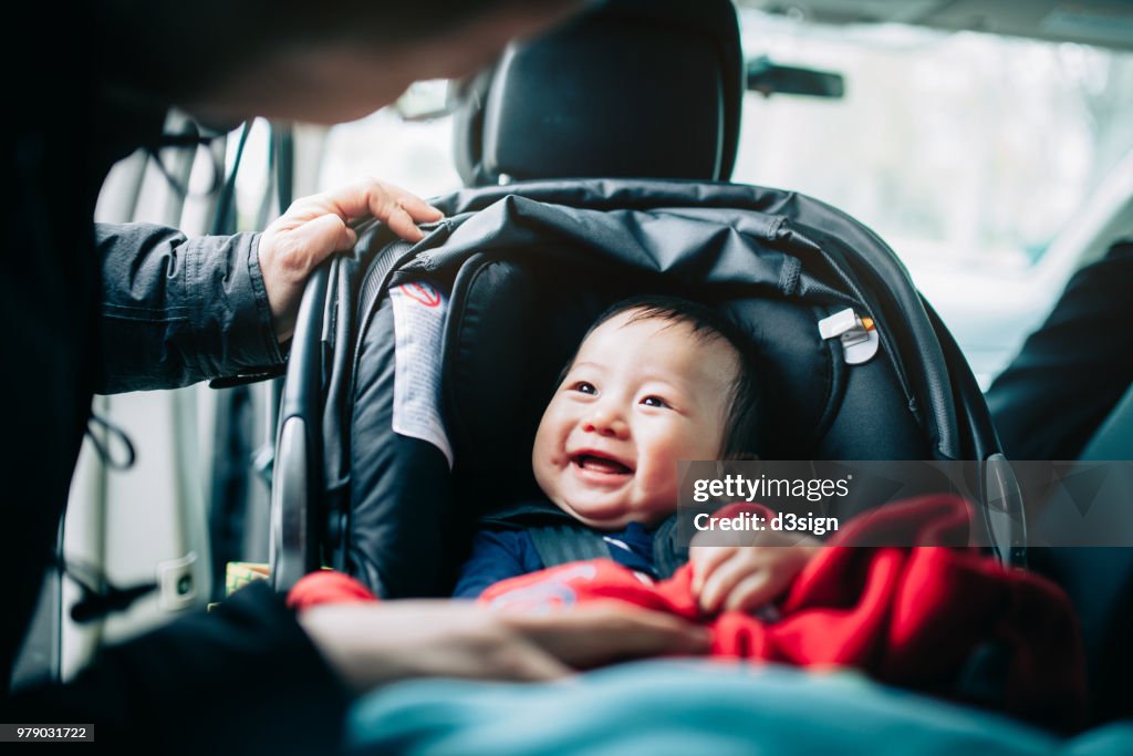 Close up of mother taking care of cute smiling baby on car seat in car