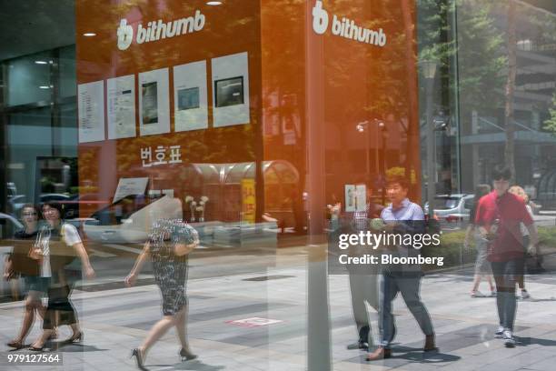 Pedestrians are reflected in the window of a Bithumb exchange office in Seoul, South Korea, on Wednesday, June 20, 2018. Virtual currencies dropped...