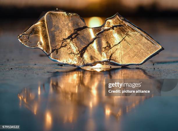March 2018, Germany, Falkenhagen: A piece of ice lies on the frozen 'Schwarzer See' at sunset. The lake is completely frozen with a ten centimetre...