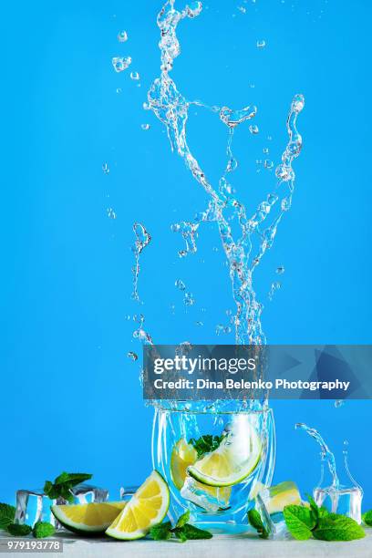 dynamic water splash with a glass of mojito or lemonade on a bright blue background. refreshing summer drink concept with copy space. - splashing cocktail stock pictures, royalty-free photos & images