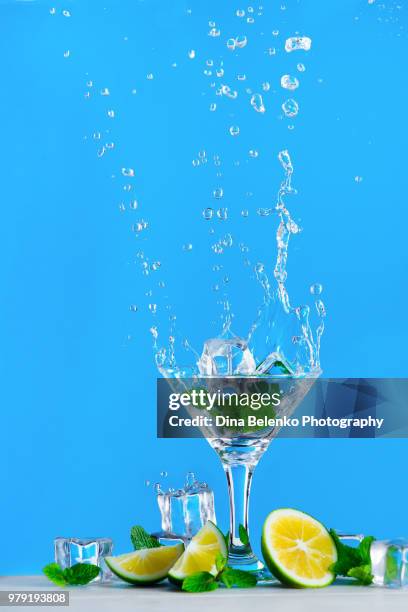 dynamic water splash with a glass of mojito or lemonade on a bright blue background. refreshing summer drink concept with copy space. - khabarovsk krai stock pictures, royalty-free photos & images