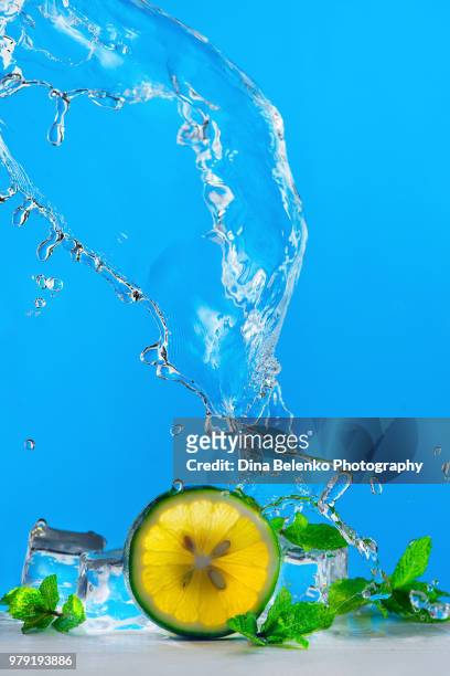 lime slice, ice, mint leaves and a dynamic water splash of mojito or lemonade on a bright blue background. refreshing summer drink concept with copy space. - khabarovsk krai stockfoto's en -beelden