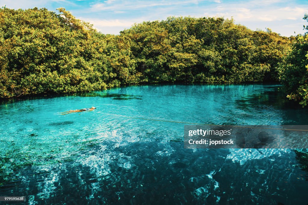 Woman floating in an open cenote in Tulum, Mexico