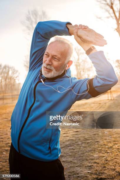 uomo maturo che allunga le braccia nel parco pubblico - winter sport foto e immagini stock