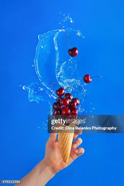 ice cream cone filled with ripe cherries with a dynamic water splash. sweet dessert in a hand against a bright blue background. simmer concept with copy space. - ハバロフスク地方 ストックフォトと画像
