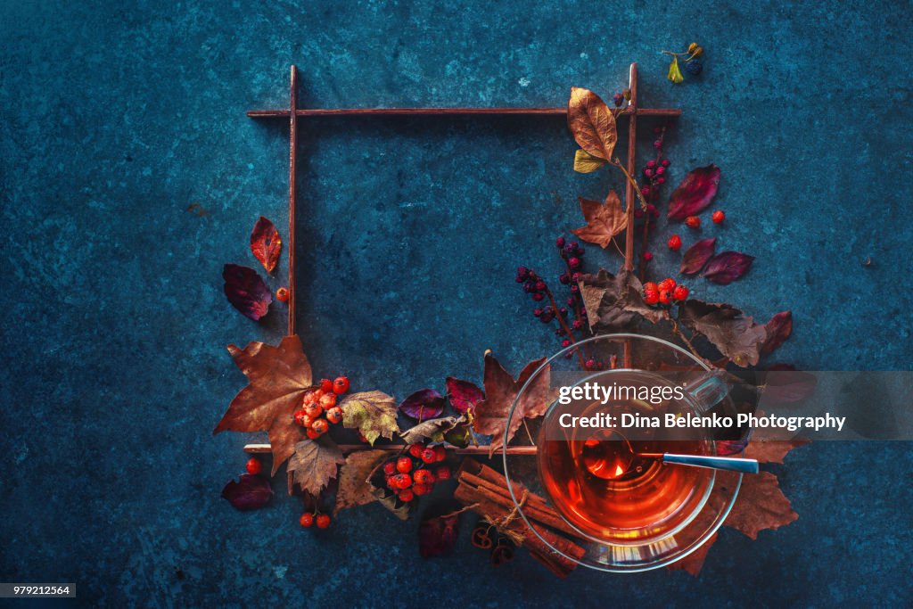 Autumn hot tea with a glass tea cup on a stone background with a square wooden frame and maple leaves. Artist study flat lay. Fall drink still life with copy space.