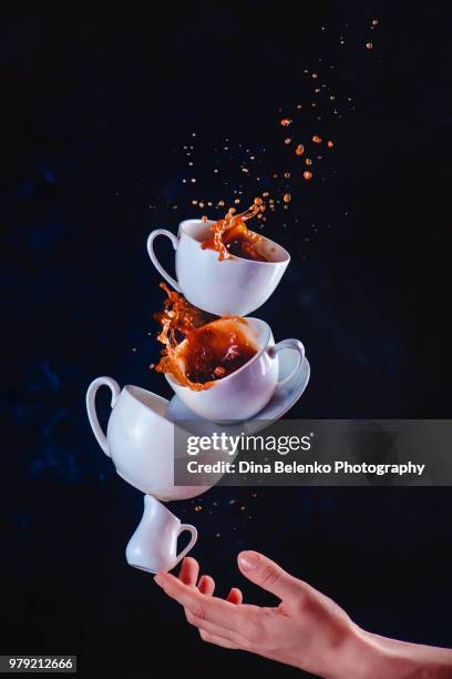 coffee cups stack with a dynamic splash balancing on a tip of a finger. high-speed food photography in motion. dark background with copy space - khabarovsk krai stockfoto's en -beelden